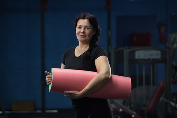 Senior woman at the gym holding a pink yoga mat. close-up. copy space.