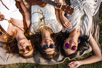 Three cute hippie girl lying on the plaid outdoors, best friends having fun and laughing, play...