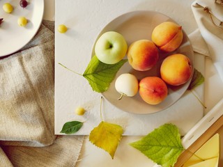 Peaches, apples, plums, leaves on plates on a light background, top view, summer, autumn season, fruit harvest, lifestyle, healthy food