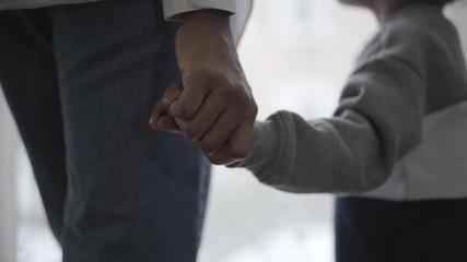 African american woman holding hand of her small cute son showing love in their house. Close up