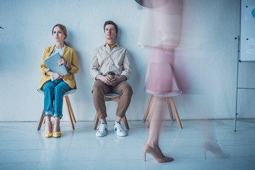 Fototapeta premium handsome man with paper cup sitting near attractive employee holding folder