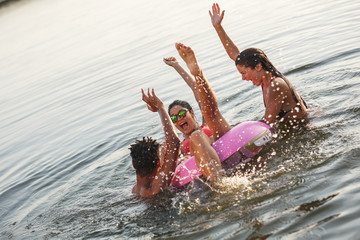 Group of friends swimming and having fun in the lake.Female sitting on air mattress drinks lemonade and having fun with friends.