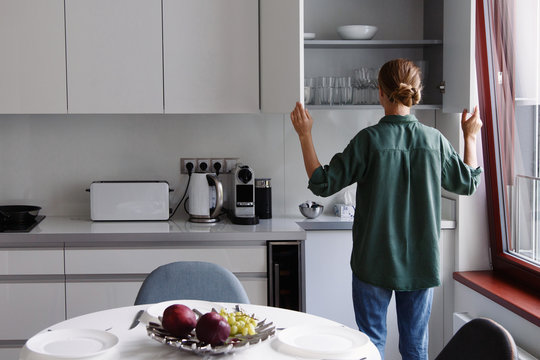 Young Girl Putting Away Cup In Cabinet In Kitchen