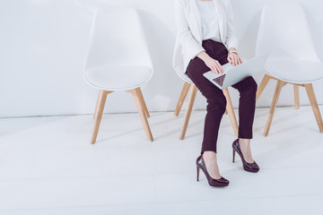 cropped view of woman sitting on chair and using laptop