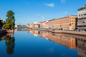 Obraz premium View of the Fontanka river with with English bridge in the distance, profitable houses on the waterfront and their mirror image in the water. Saint Petersburg, Russia