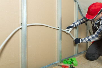 Electrician at work - installing electricity wire into plasterboard wall in attic