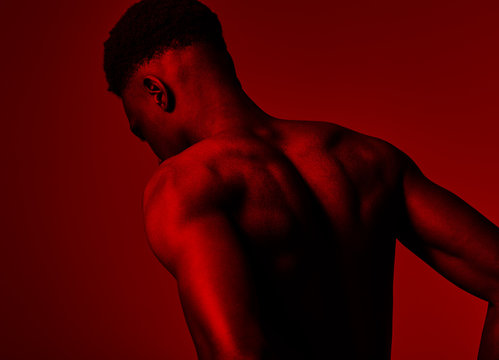 A shirtless man photo from behind under red light.