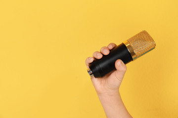 Child holding microphone on color background, closeup of hand. Space for text