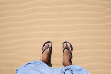 Male feet in flip flops standing at the desert in summer.