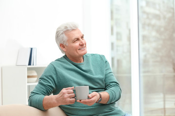 Portrait of mature man with cup of drink on sofa indoors