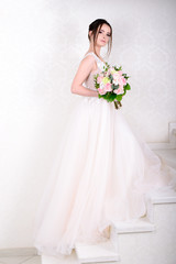 Slim beautiful woman wearing luxurious wedding dress over white studio background. Gorgeous bride holding flowers.