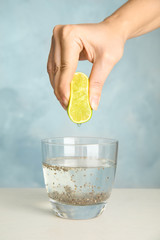 Young woman squeezing lime into glass of water with chia seeds on table, closeup