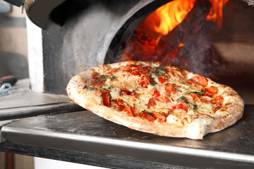 Taking out tasty pizza from oven in restaurant kitchen - Powered by Adobe