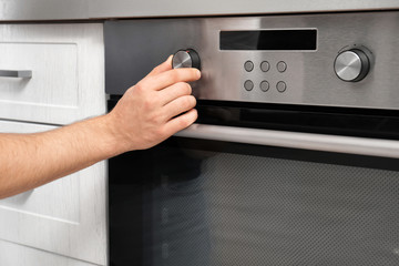 Young man adjusting oven settings in kitchen, closeup