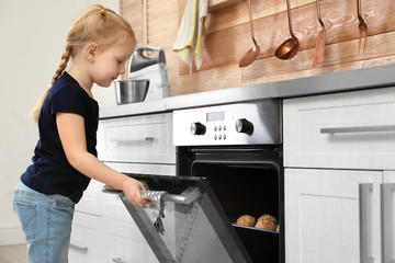 Little girl checking cookies in oven at home