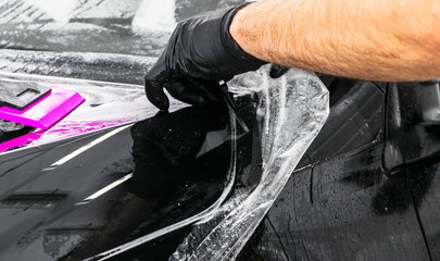 Car wrapping specialist putting vinyl foil or film on car. Protective film on the car. Applying a protective film to the car with tools. Car detailing. Transparent film. Car paint protection. Trimming