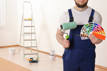 Male decorator with paint roller and color palette samples in empty room, closeup. Space for text