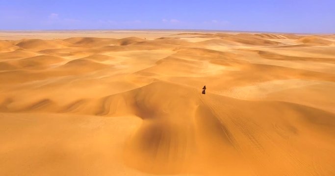NAMIB-NAUKLUFT NATIONAL PARK, NAMIBIA. Top aerial 4K view of huge area covered in yellow hot sand. Two men wearing helmets ride along beautiful arid landscape.