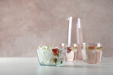 Bowl with floral ice cubes and glasses of water on table