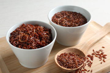 Board with boiled and uncooked brown rice on table, closeup