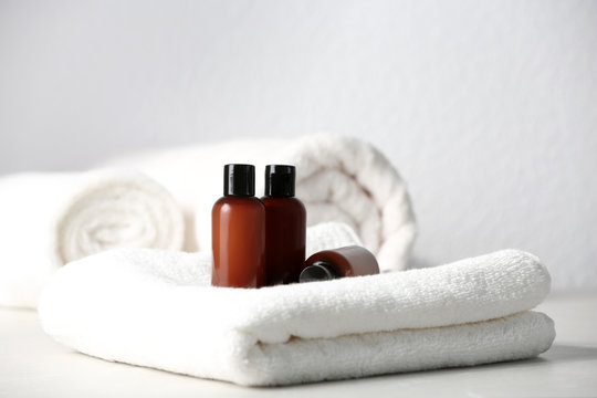 Mini bottles with cosmetic products and towels on table against light background. Hotel amenities