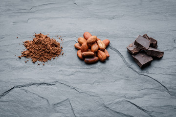Organic cacao beans, cacao powder and chocolate on a black stone background.