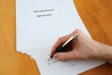 Non-disclosure agreement and hand with pen about to sign it on wooden table