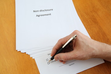 Non-disclosure agreement and hand with pen about to sign it on wooden table