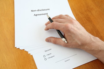 Non-disclosure agreement and hand with pen considering to sign it on wooden table