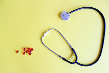 Medical stethoscope, stethoscope and red pills on a yellow background. Pills and treatments.