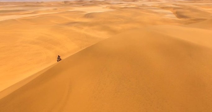 NAMIB-NAUKLUFT NATIONAL PARK, NAMIBIA. Tourist wearing black tracksuit rides ATV within an ocean of enormous red dunes. Aerial 4K view of dramatic landscape with terracotta dunes.