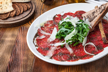 Close up view on veal carpaccio with parmesan and toast. Raw beef tenderloin with sauce on wooden...