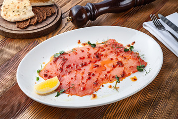 Delicious view on tuna carpaccio on white plate. Close up view on Raw tuna tenderloin with sauce on wooden background with copy space. Fresh italian appetizer. Seafood italian mediterranean cuisine