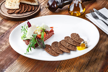 Close up view on fresh beef tartare with bread, egg and microgreen in white plate. Homemade tartare veal on wooden background with copy space. Served food for menu or recipe. Italian cuisine appetizer
