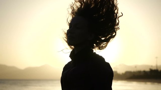 Slow Motion Close up silhouette of Young Woman moving her head with hair blowing in wind looking at sunset over ocean.