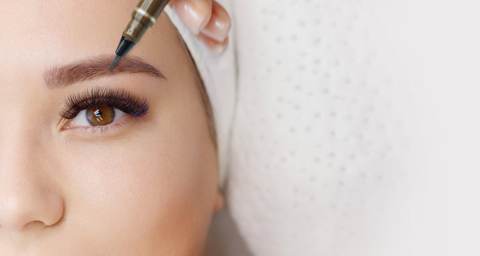 Beautiful Young Girl With Long Eyelashes Tweezing Her Eyebrows In A Beauty Salon. Woman Doing Eyebrow Permanent Makeup Correction . Microblading Brow.