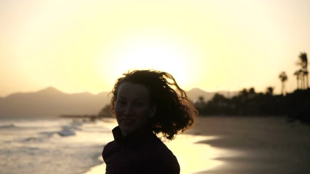 Slow Motion Close up silhouette of Young Woman jogging on a beach with hair blowing in wind looking at sunset over ocean.