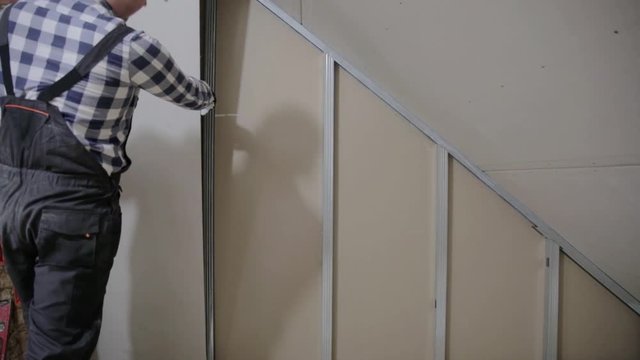 Man installing plasterboard sheet to wall for attic room construction