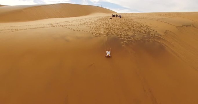 NAMIB-NAUKLUFT NATIONAL PARK, NAMIBIA. Adult tourist sliding on sand dunes. Sand sledding within bright orange dunes.