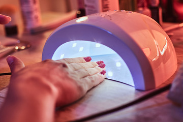 Client at manicure salon dryes gel nails in UV light