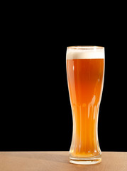 Light beer on the table on a black background. Tall beer glass.
