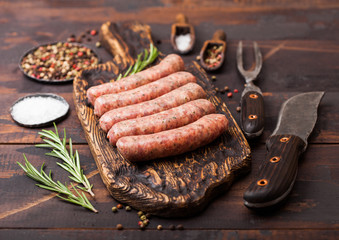Raw beef and pork sausage on old chopping board with vintage knife and fork on dark wooden background.Salt and pepper with rosemary. - obrazy, fototapety, plakaty