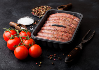 Raw beef and pork sausage in plastic tray with vintage fork on black background.Salt and pepper with tomatoes and rosemary.