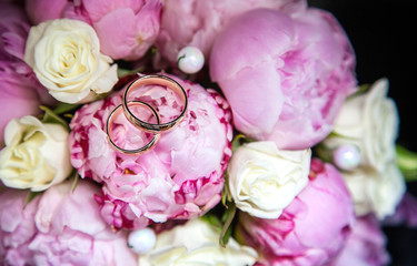 Wedding rings on the bride's bouquet from the pink and white roses. Close-up. On the photo, there are no people only golden rings and flowers. Background is blurred.