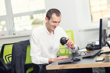 Young male sitting in the office at work asks a question magic ball with prediction. Search for an answer.