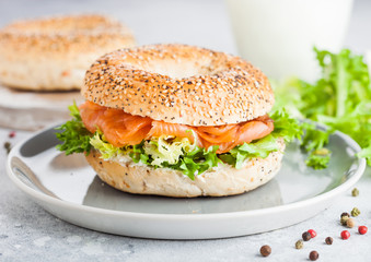 Fresh healthy bagel sandwich with salmon, ricotta and lettuce in grey plate on light kitchen table background. Healthy diet food. Glass of milk and fresh vegetables