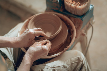 High angle of clay master's dirty arms working on potter's wheel