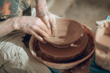 High angle of clay master's dirty arms working on potter's wheel
