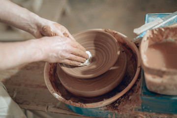 High angle of clay master's dirty arms working on potter's wheel