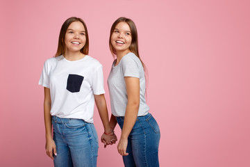 Bright two young twin sisters with beautiful smile walk over pink background.